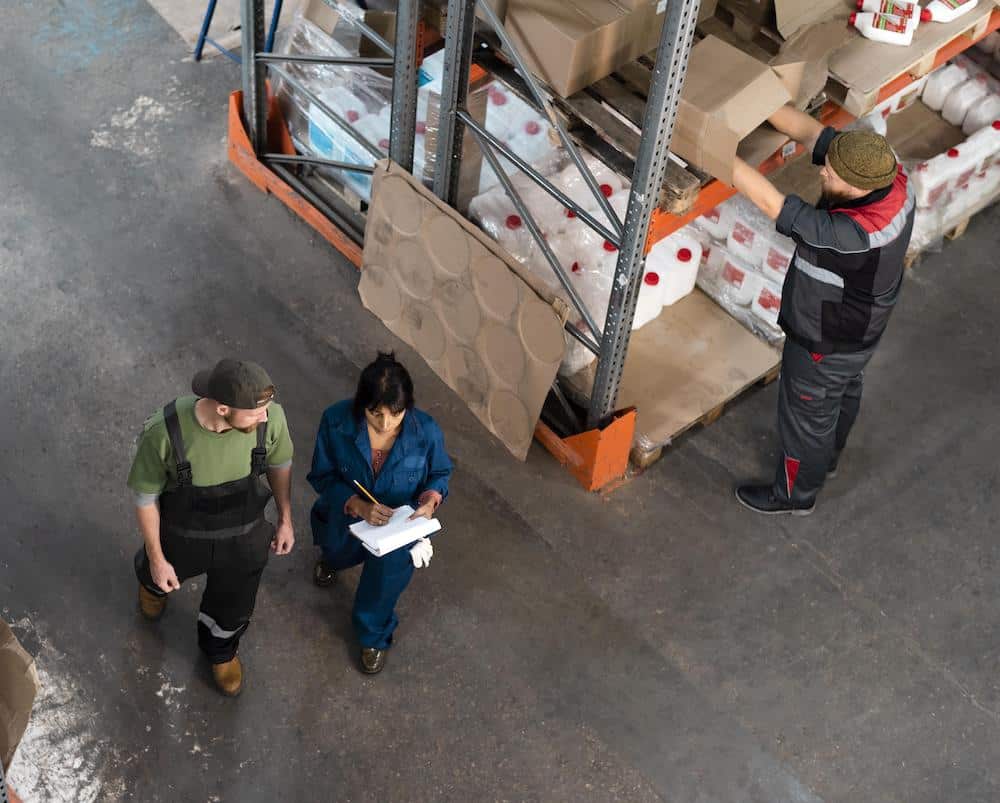 Warehouse workers conducting inventory inspection with forklift and storage shelves