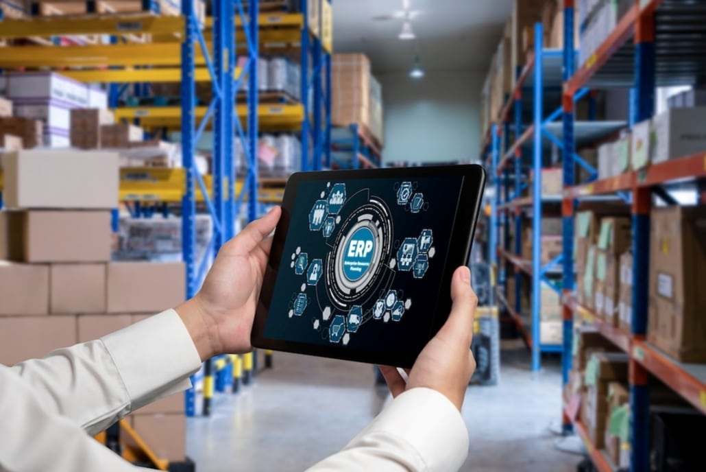 executive holidng a tablet in a warehouse showing a graphic on the screen with ERP in the middle surrounded by process icons