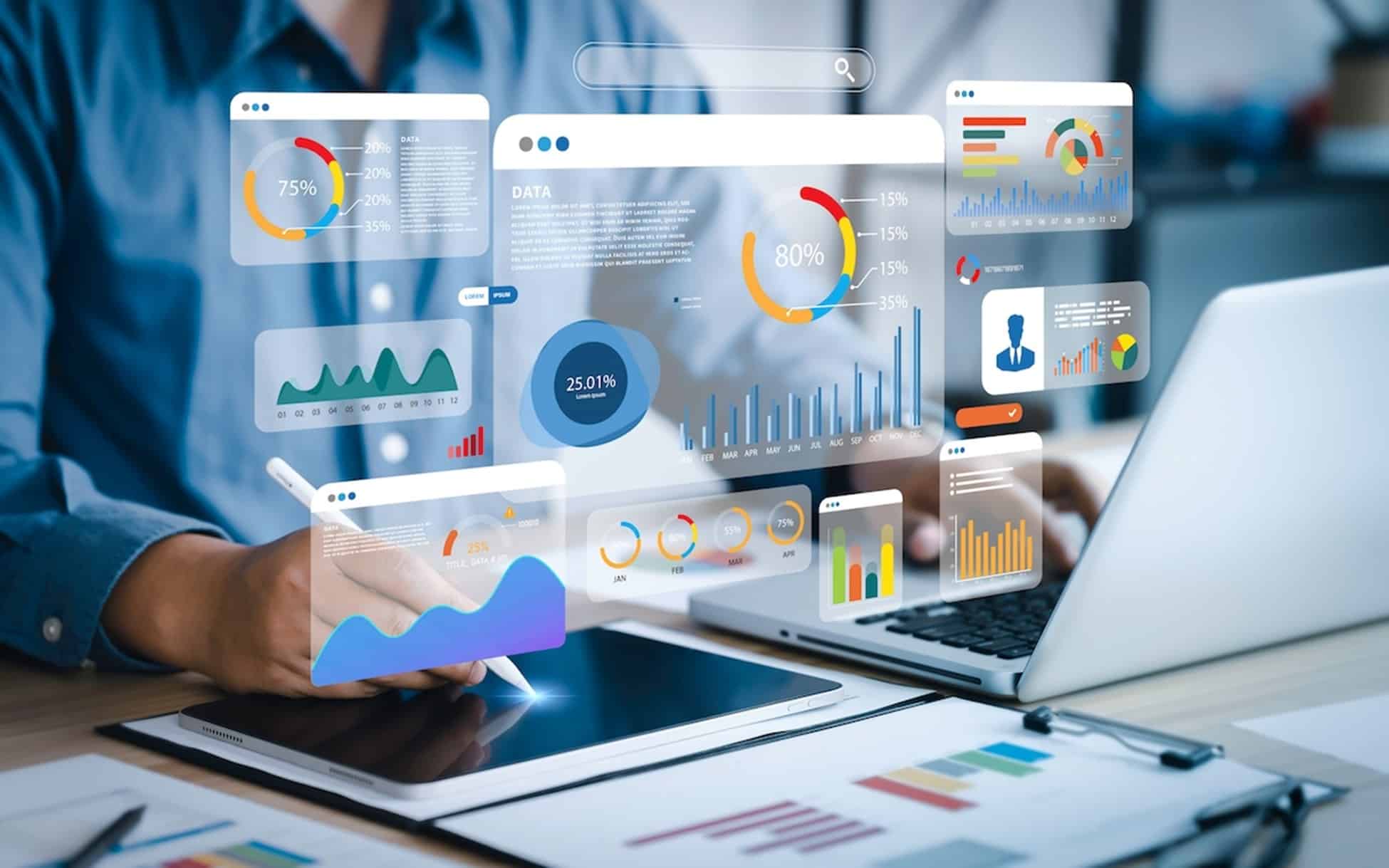 person on a laptop and tablet with icons floating in the showing what they are working on different charts and graphs